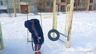 Naked tomboy in a fur coat swings on a swing in winter