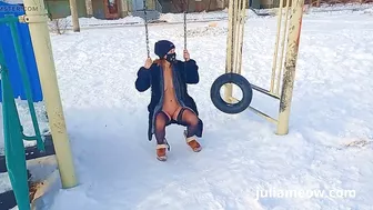 Naked tomboy in a fur coat swings on a swing in winter