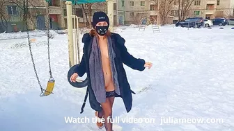 Naked tomboy in a fur coat swings on a swing in winter